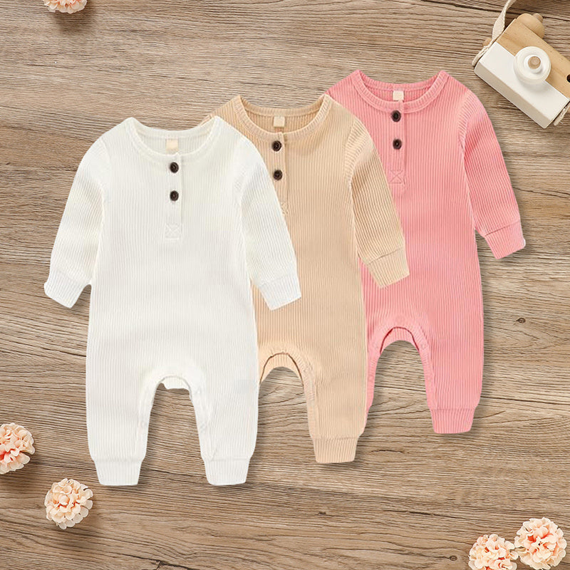 Three baby rompers in white, beige, and pink on a wooden surface with small flowers around.